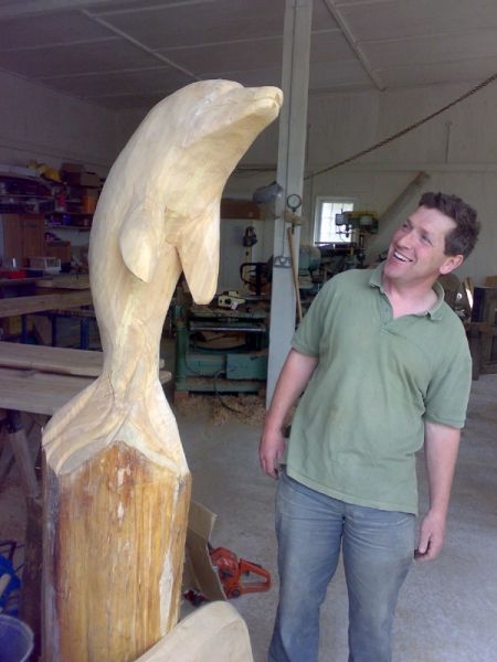 man looking at wooden dolphin carving on a plinth