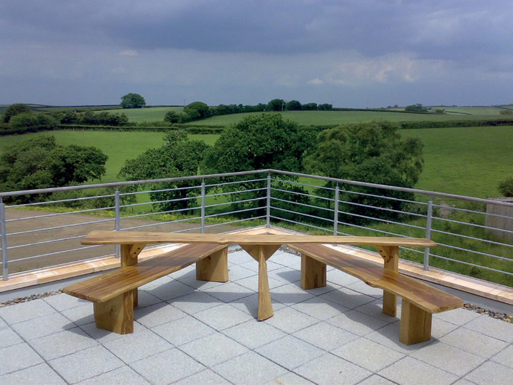 Wooden All Ability Picnic Table Bench installed on paving overlooking fields and woodland